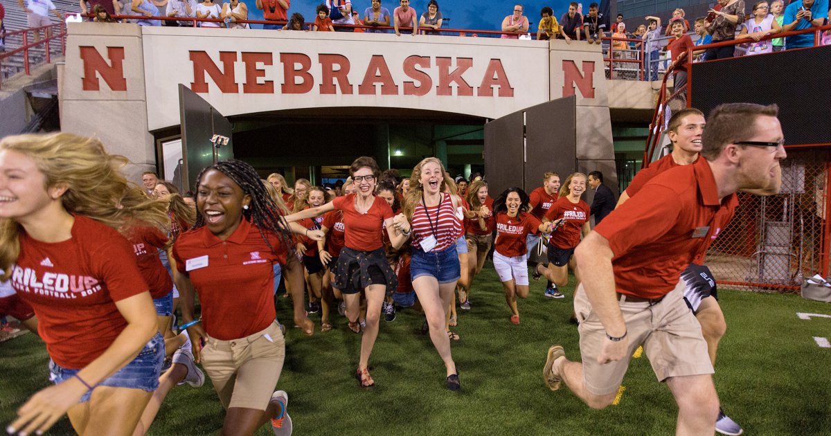 A photograph of students running out of the tunnel at Memorial Stadium at the University of Nebraska-Lincoln, they are all wearing Nebraska Husker gear.